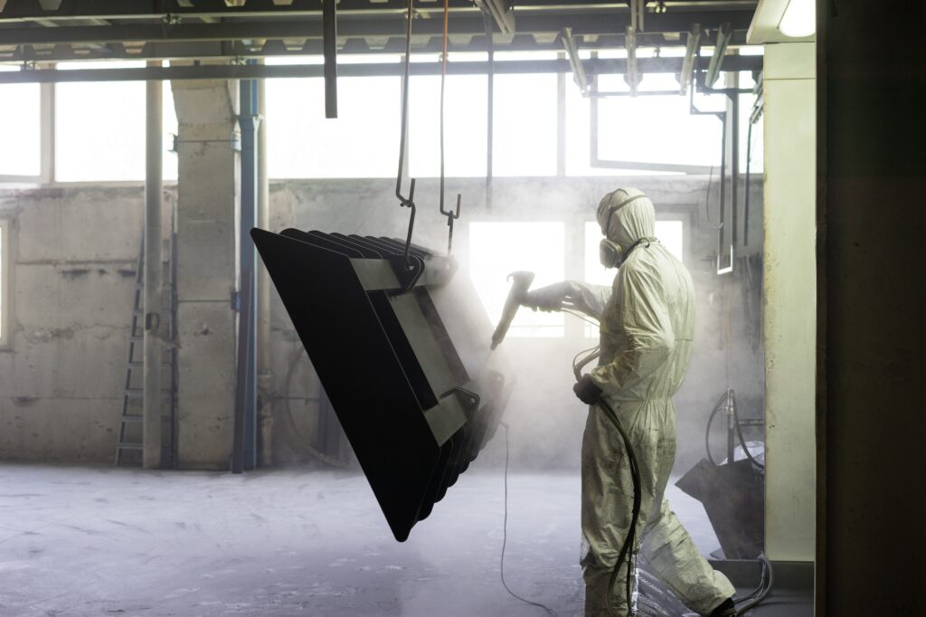 worker sand blasting a metal crate
